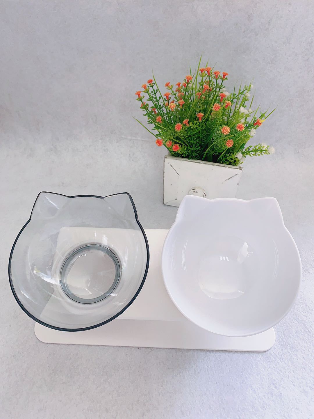 Cat-shaped bowls on a stand with a small plant on a light gray background